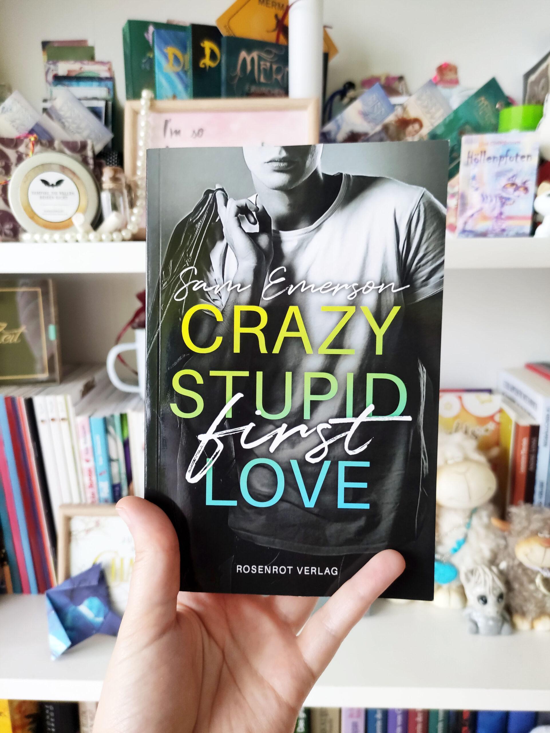 Das Buch Crazy Stupid First Love wird vor ein Bücherregal gehalten