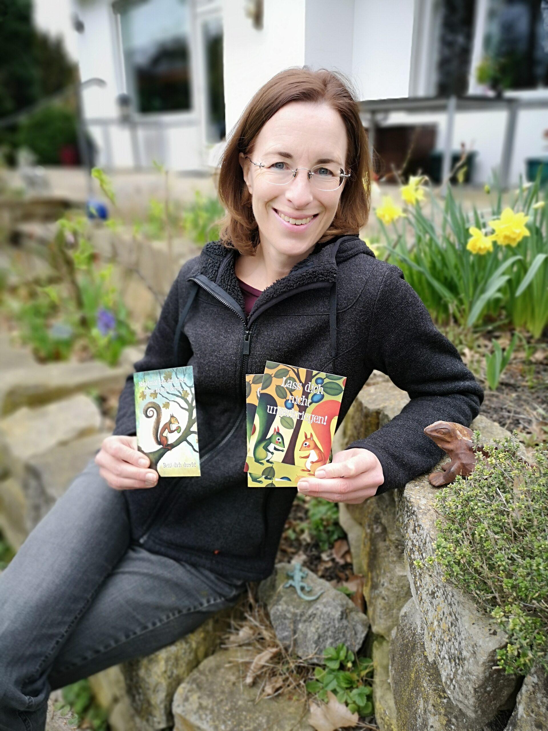 Die Autorin Patricia Strunk hält Postkarten ihres Buches Geschichten aus dem Garten hoch