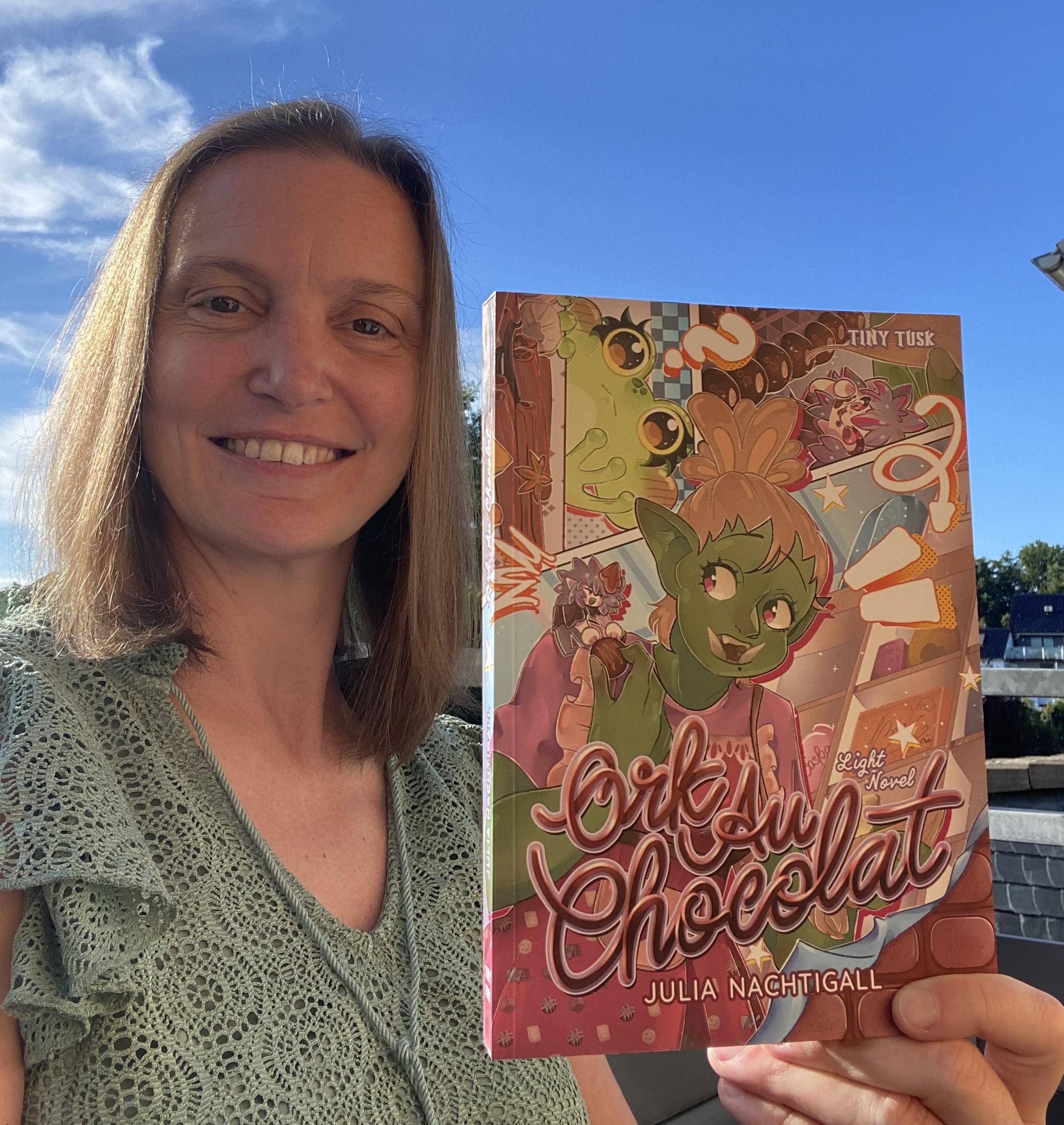 Autorin Julia Nachtigall hält für ein Interview ihr Buch Ork au Chocolat unter freiem Himmel in die Kamera