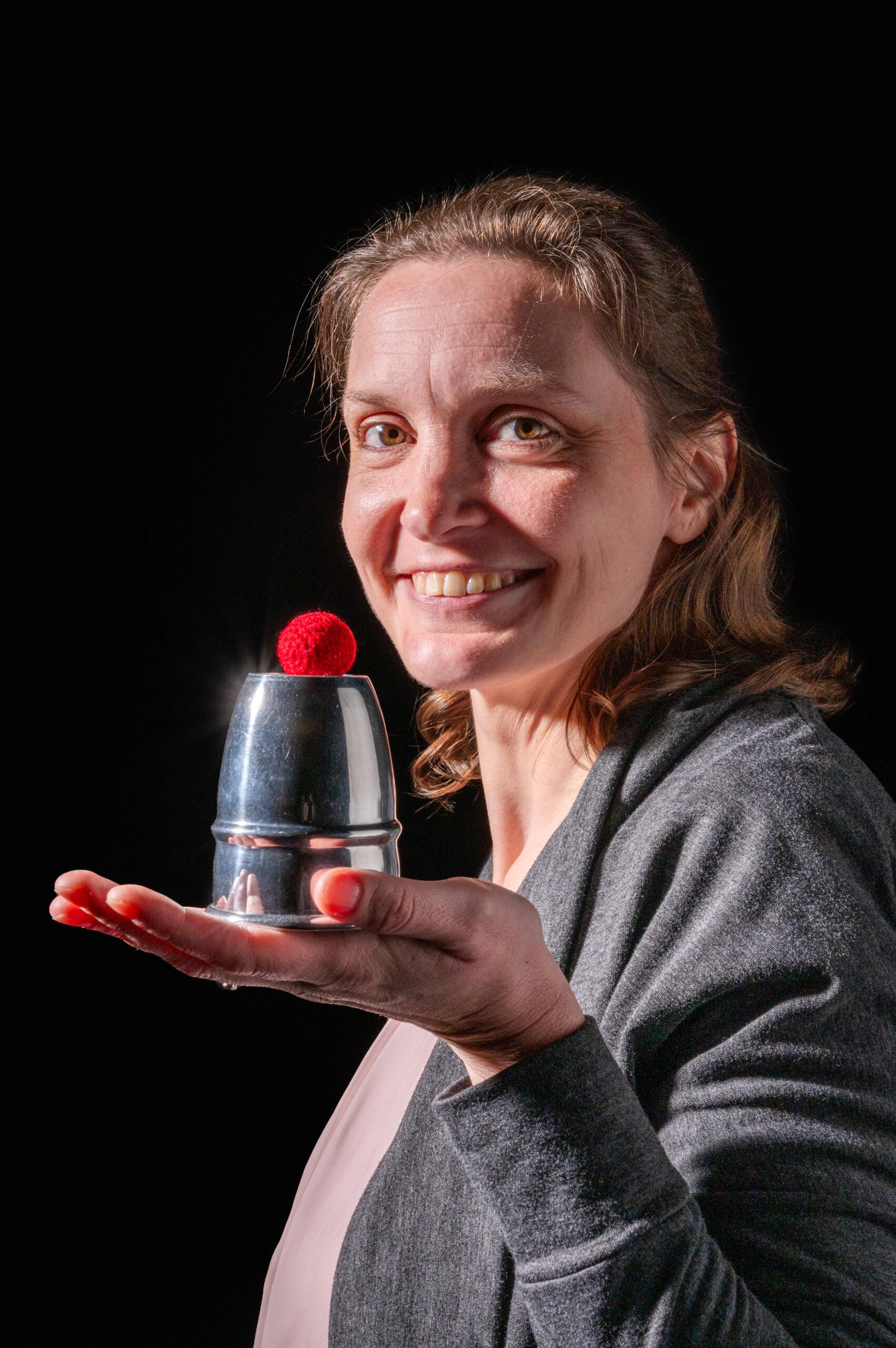Autorin Julia Nachtigall hält für ein Interview Zauberzubehör in der Hand und steht dabei vor einer schwarzen Wand