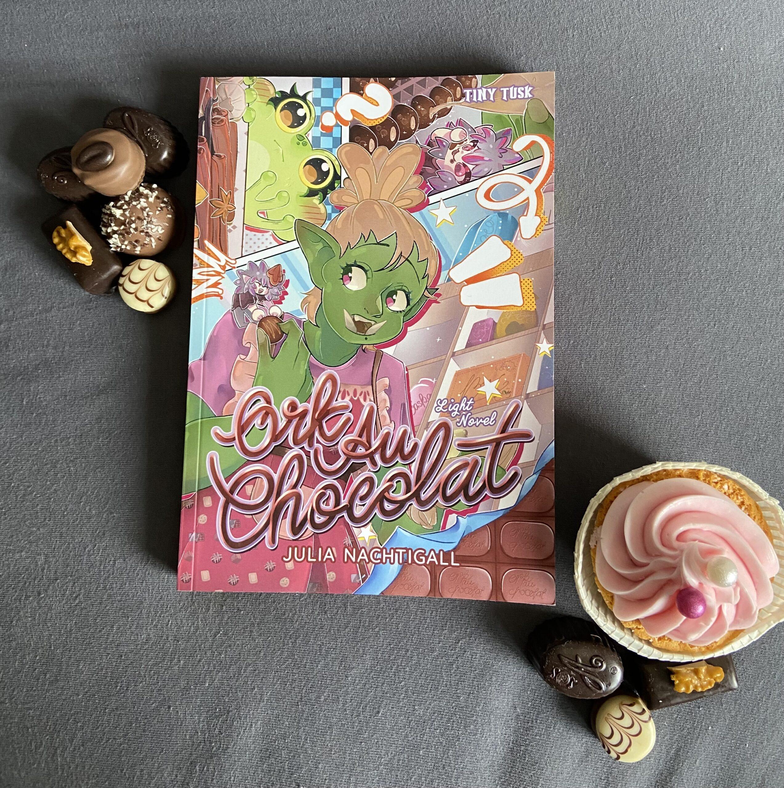 Das Buch Ork au Chocolat liegt mit Süßigkeiten auf grauem Hintergrund