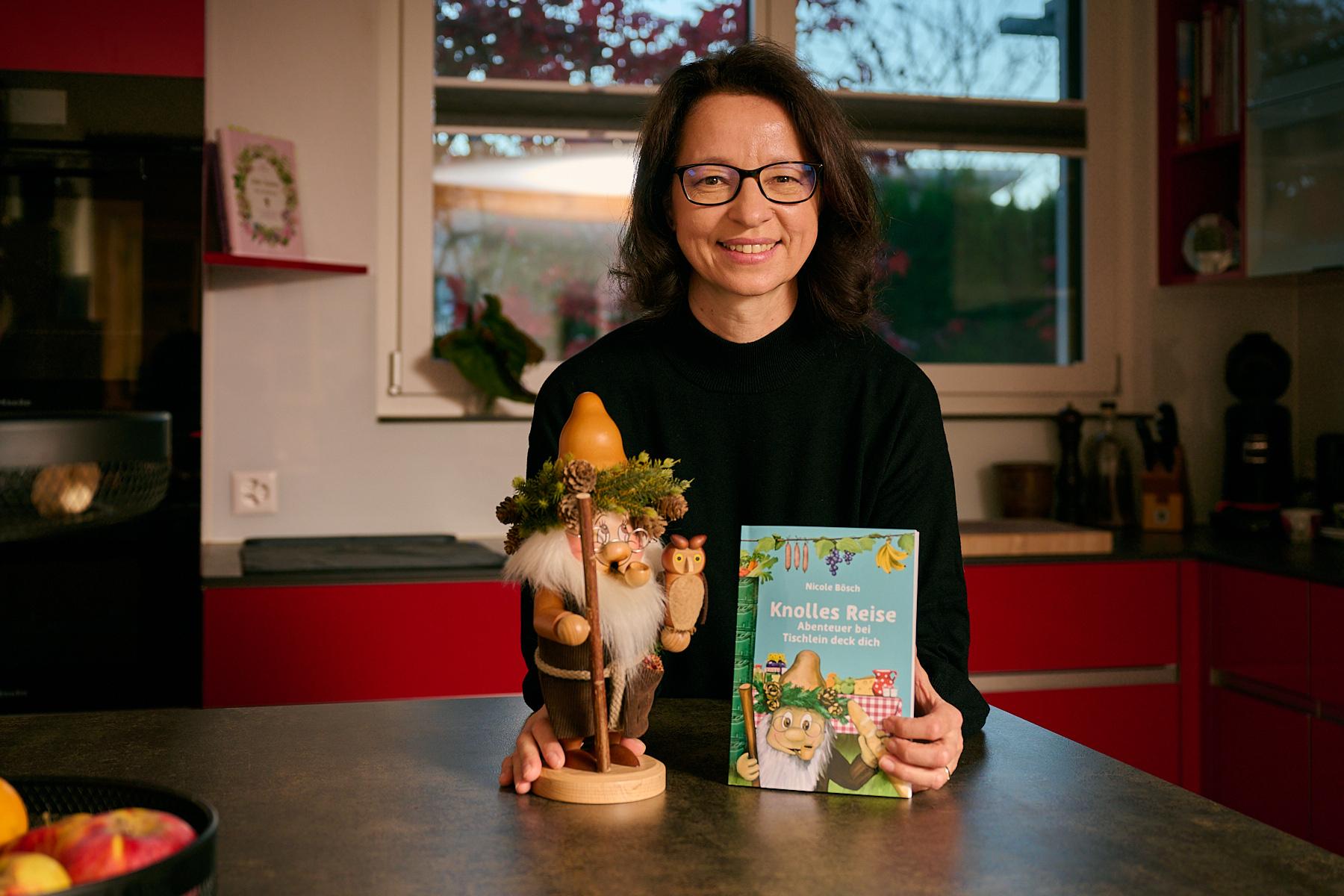 Die Autorin Nicole Bösch präsentiert für ein Interview ihr Buch Knolles Reise Abenteuer bei Tischlein deck dich in einer Küche und hält Knolle selbst in der Hand